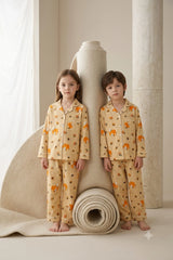 Twin boy and girl wearing matching beige and orange woodland fox print linen button-down pajama sets.