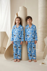 Twin girl and boy wearing matching sky blue linen button-down pajama sets featuring an illustrated zebra and rainbow cloud print with white piping.