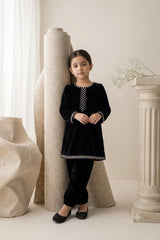 Young girl wearing a midnight black micro-velvet kurti and trouser set embellished with delicate white pearls along the neckline, cuffs, and hem paired with black khussas.