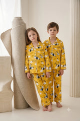 Twin girl and boy wearing matching golden mustard yellow linen button-down pajama sets featuring a playful zebra and cloud print with white piping.