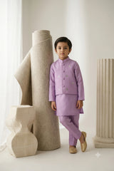 Young boy wearing a soft lilac raw silk kurta pajama set with a floral-embellished waistcoat and gold khussas for wedding celebrations.