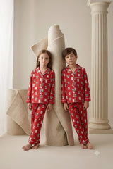 Boy and girl wearing matching scarlet red linen button-down pajama sets featuring an adorable panda and teddy bear print with white piping.