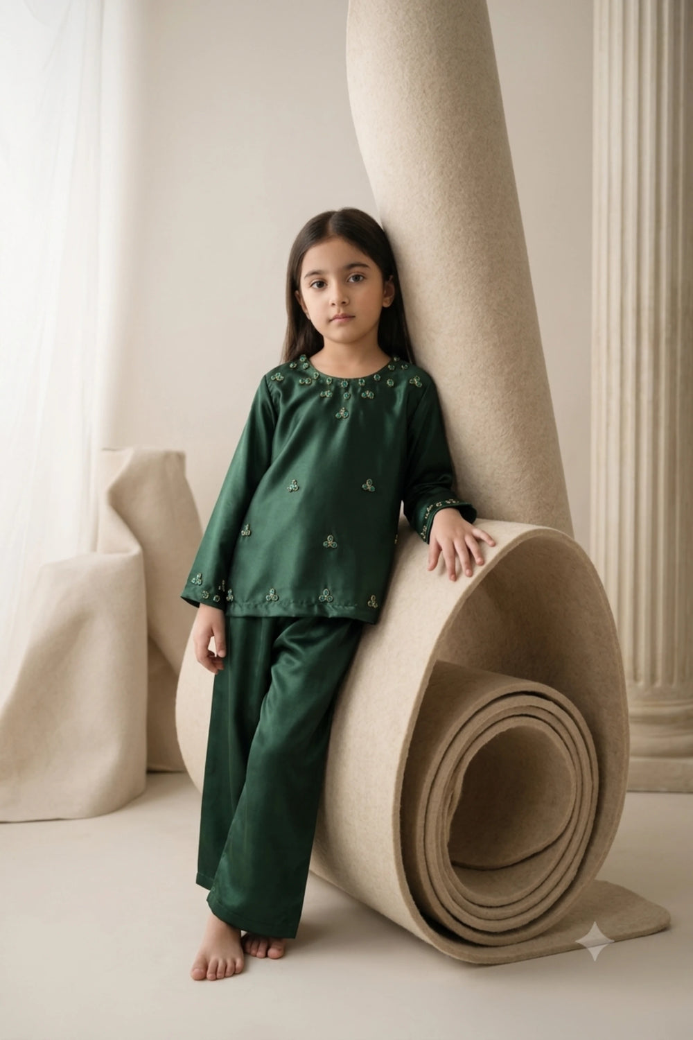 Young girl standing leaning on a coiled roll wearing a rich emerald pine green shamoz silk kurti and trouser set with floral crystal neckline embellishments.