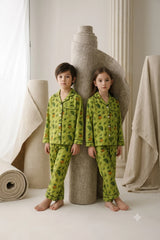 Twin boy and girl wearing matching lime green linen button-down pajama sets featuring a rainy woodland umbrella and leaf print with dark green piping.