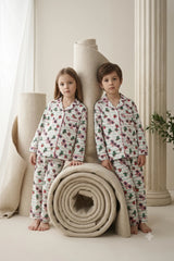 Flat lay of unisex kids striped linen button-down pajama set featuring a playful print of watermelons, sunglasses, and cacti with pink piping.